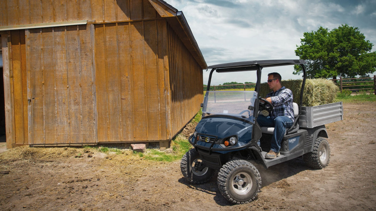 Close-up of a black off-road utility vehicle with large knobby tires on a dirt ground, with a person's foot visible stepping onto the vehicle.